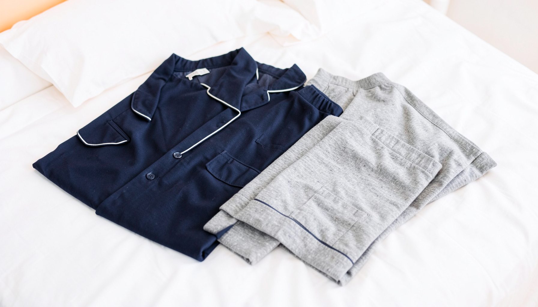 Classic mens pajama sets in deep navy and grey laid out on crisp white bedding