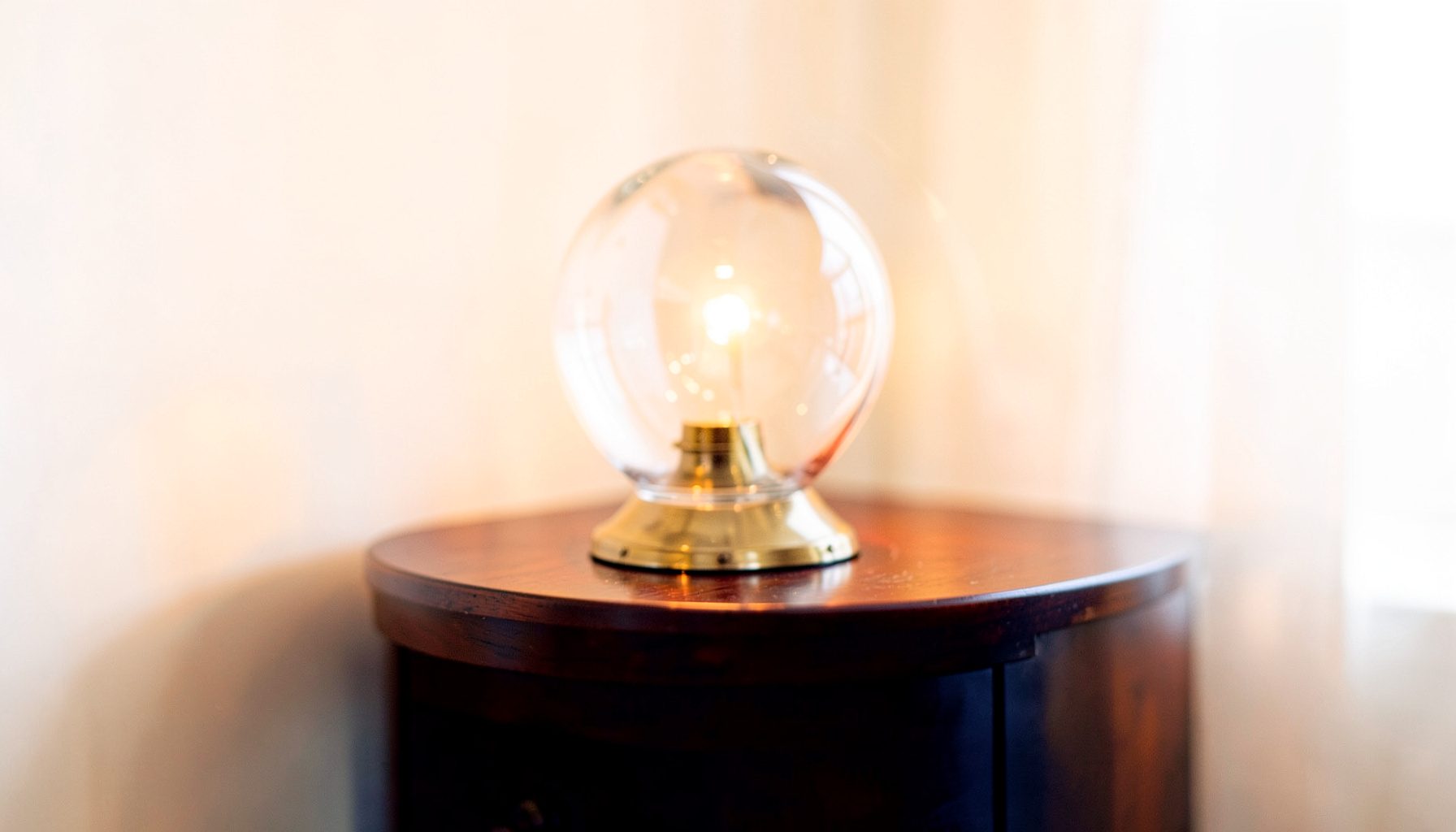 A warm, softly lit interior with a crystal ball lamp casting gentle reflections across a polished wooden side table, deep navy and amber tones