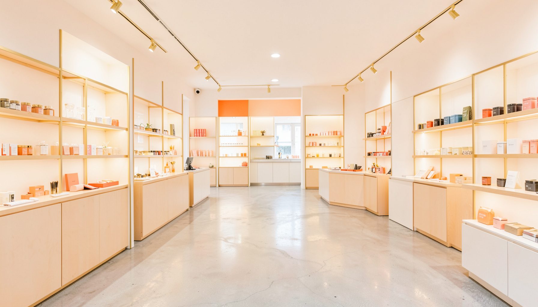 Modern boutique interior with polished concrete floors, brass fixtures, and neatly arranged product displays in warm ambient lighting.