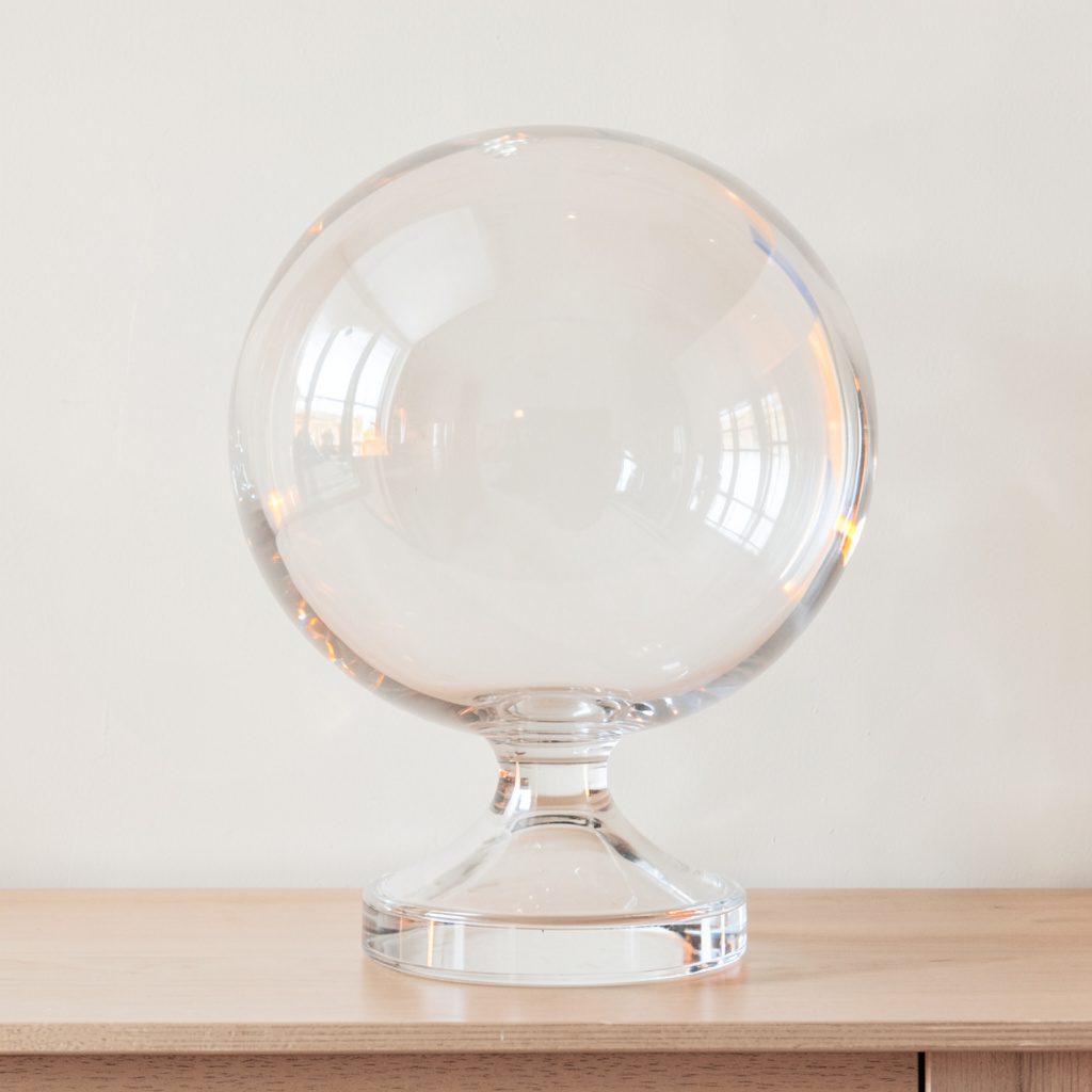 A large crystal ball lamp base, substantial clear sphere with rich refractions, placed on a console against a muted wall