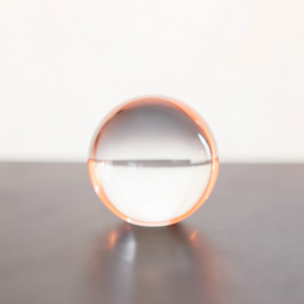 A small crystal ball lamp base on a dark surface, clear glass sphere catching soft ambient light, elegant and minimal