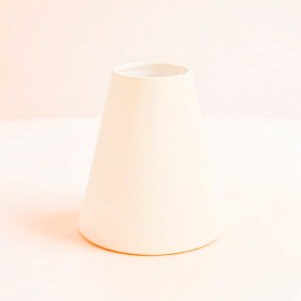 A small card lamp shade in crisp off-white, clean tapered shape, resting on a bright surface
