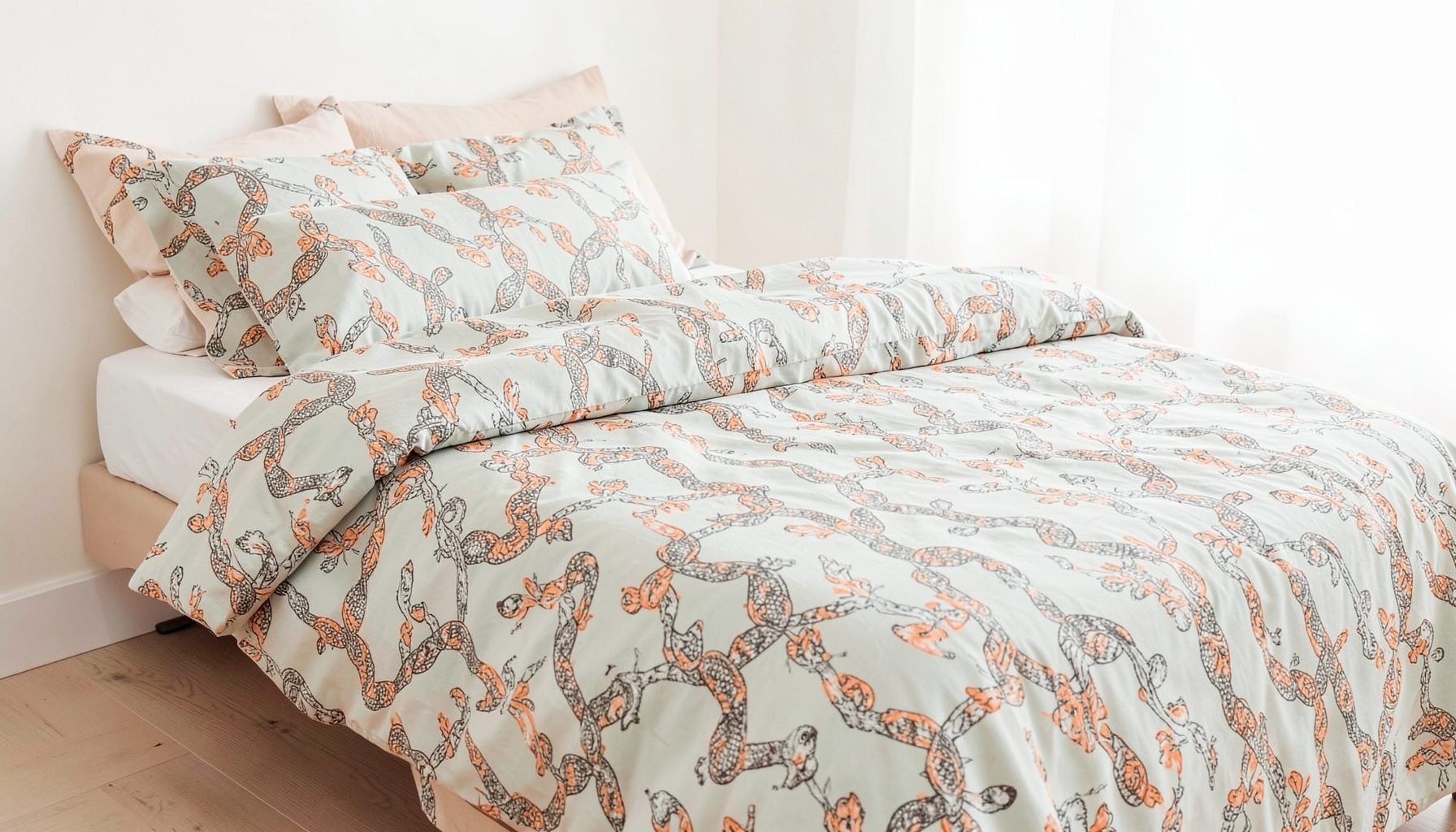 A single bed with a snake-pattern duvet set, muted sage and stone tones